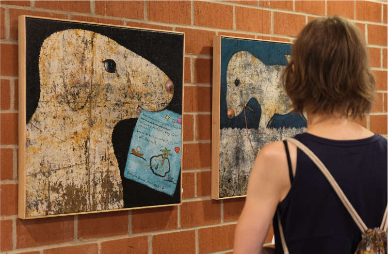 Eine Besucherin der Vernissage betrachtet sich die Werke „Ausflug II“ (rechts) und „Seemann Bruno“. (Foto: KV SÜW)