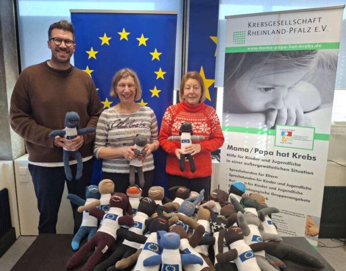 Maco Zettl, Leiter von Europe Direct Kaiserslautern, Heidi Noichl, Mitarbeiterin von Europe Direct Kaiserslautern, und Ingrid Sander aus der Kreativgruppe des Fördervereins "Mama/Papa hat Krebs" Kaiserslautern präsentieren die Sockenhasen mit ihren Europa-Pullis. (Foto: Stadt Kaiserslautern)