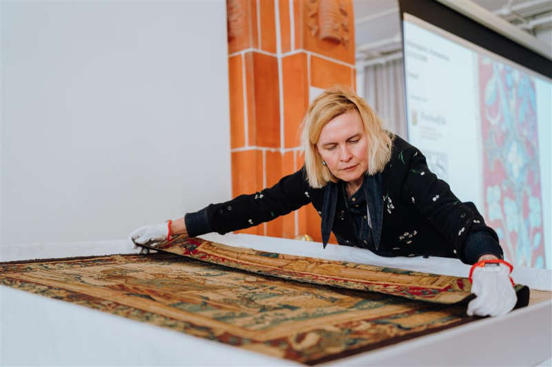 Eine Restauratorin zeigt die Rückseite des Bildteppich. (Foto: Aljosha Wohlgemuth)